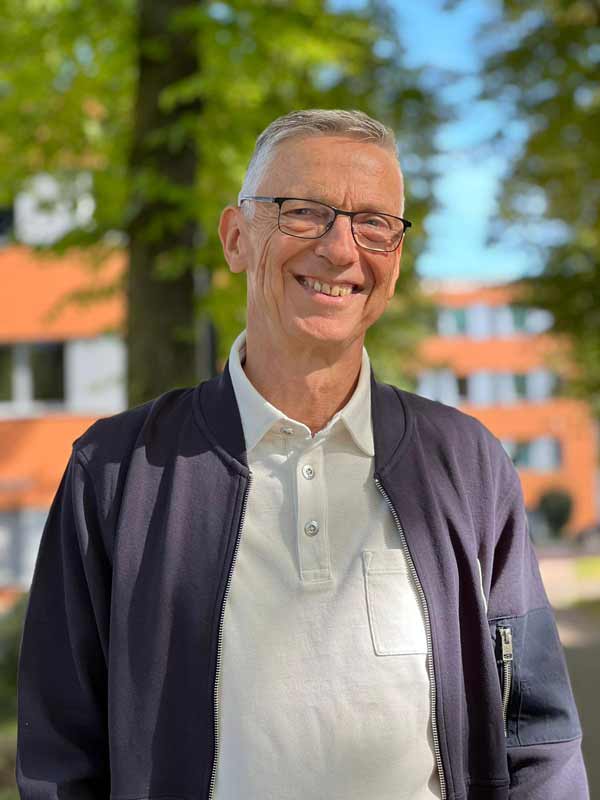 Portrait von Uwe Kreß, Trainer und Mentor, freundlich lächelnd im Freien vor einem Gebäude – Symbol für Klarheit, Professionalität und Vertrauen.