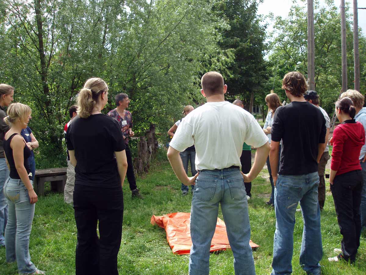 Trainer Götz Uwe Kreß steht vor einer Gruppe im Freien und leitet eine Übung an – Gruppenleitung Fortbildung mit Sicherheit und Empathie.