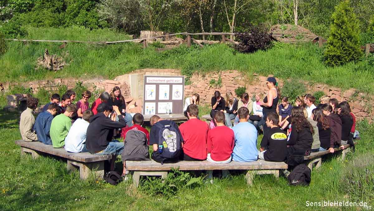 Reflexionsrunde im Hochseilgarten Worms – Schülergruppe im Sitzkreis mit Trainerin, im Hintergrund die Tafel Sicherheit geht vor