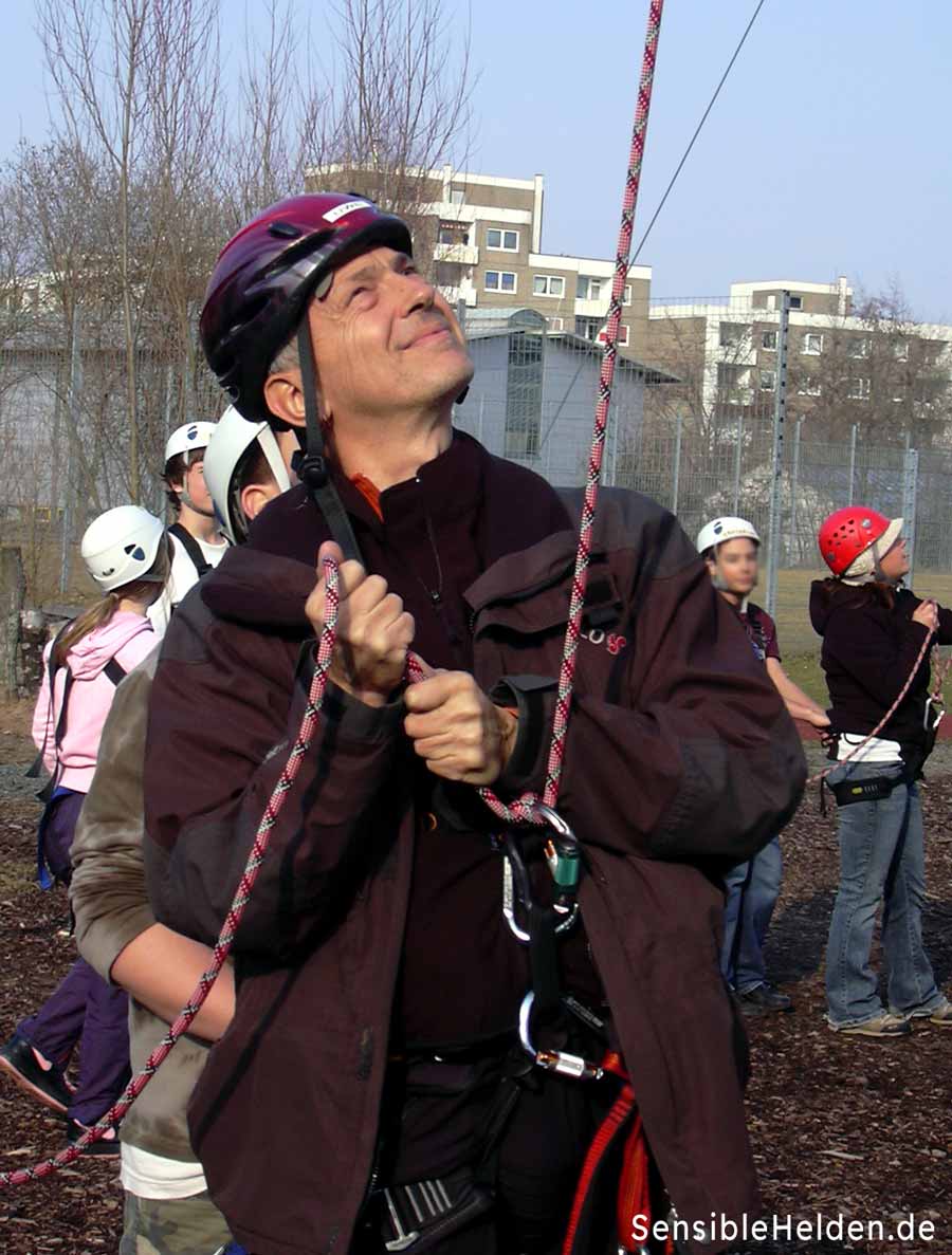 Sicherheitsausrüstung im Hochseilgarten Worms – hier Götz Uwe Kreß mit Helm, Gurt beim professionellen Sichern eines Teilnehmers