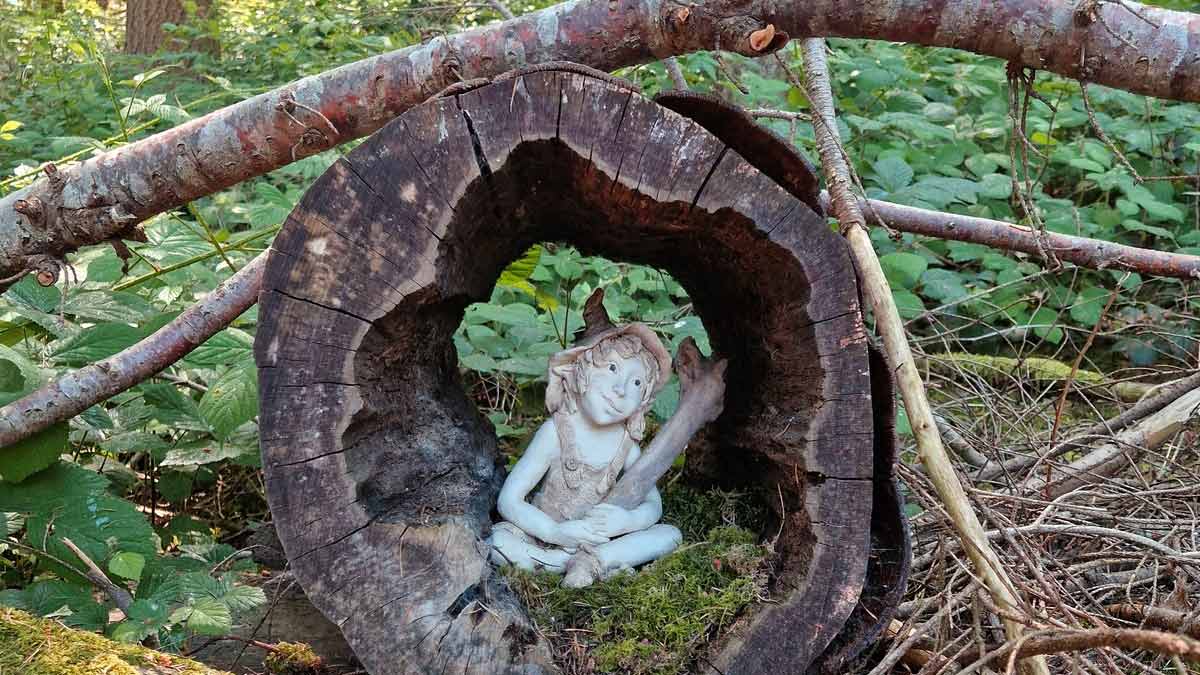 Elf im hohlen Baumstamm Kleine Elfenfigur sitzt im Rund eines hohlen, moosbewachsenen Baumstamms